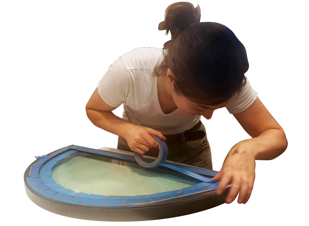 A woman masking the edges of a steel window frame with tape.