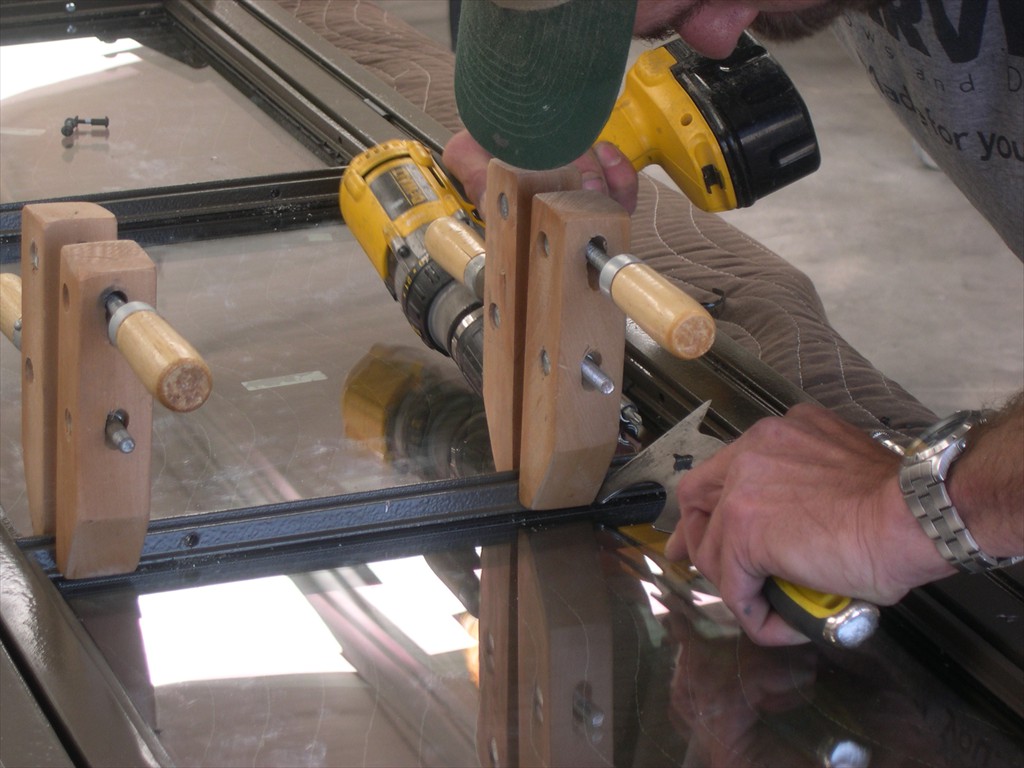 A man drills into a clamped window frame component.