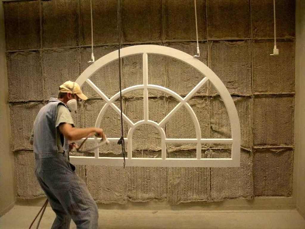 A worker paints an arched window with a spray gun.