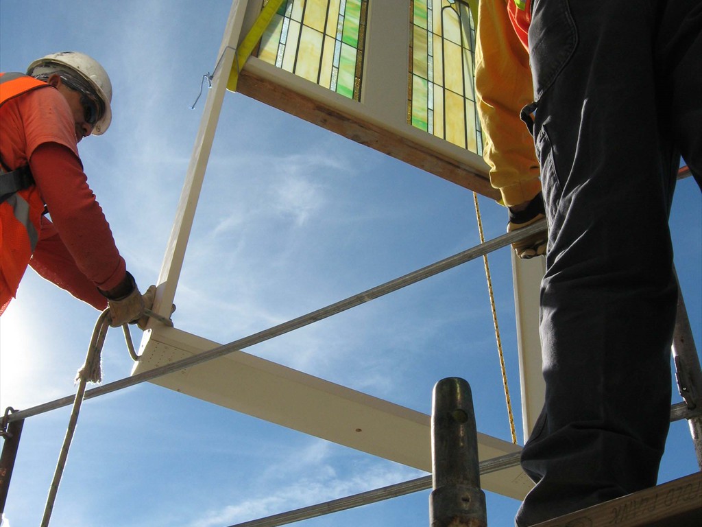 Workers guide a large stained glass window into place during installation.
