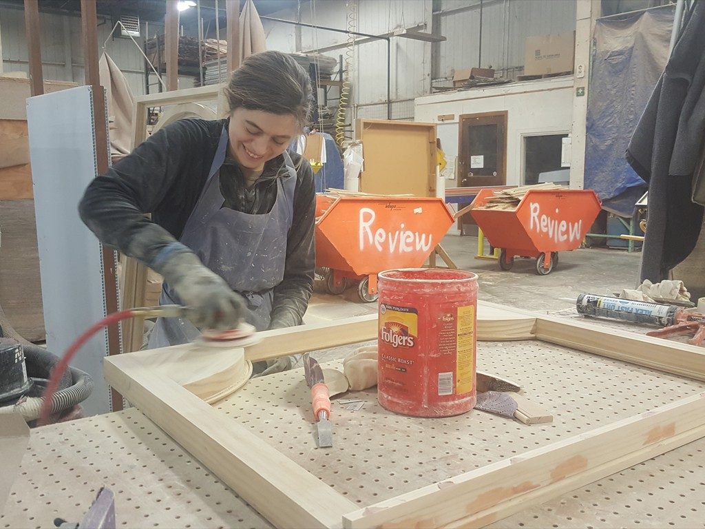 A worker sands a wood window component in the shop.