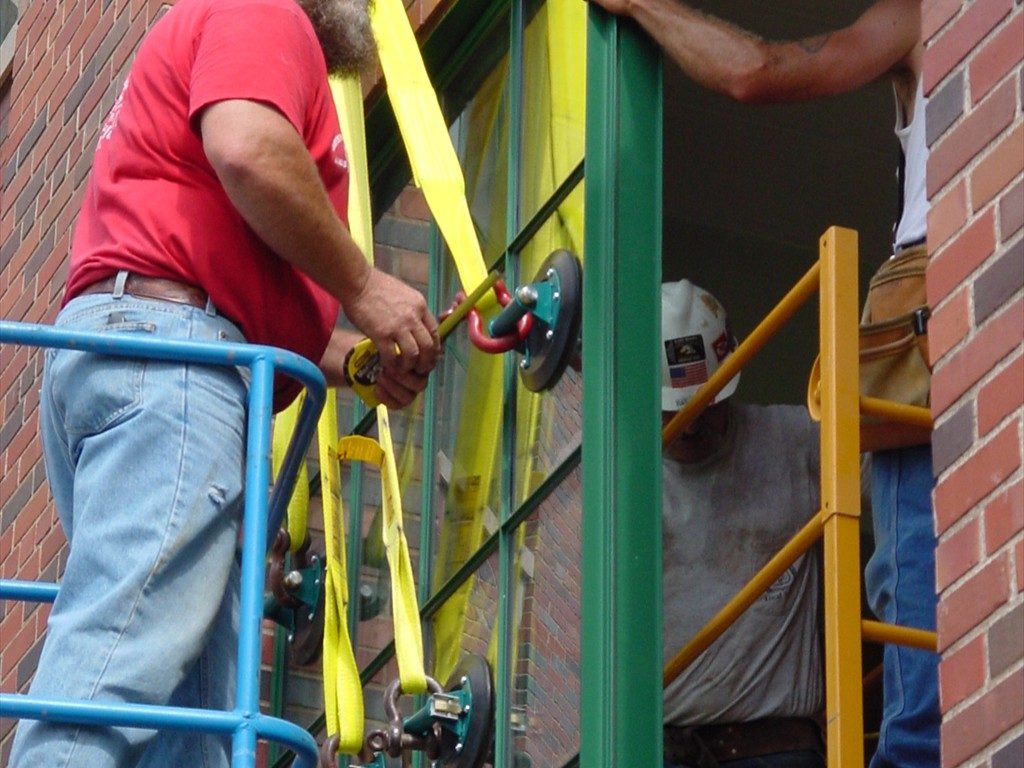 Workers guide a large aluminum window into place.