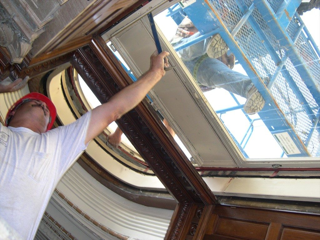 A worker prying at a window frame with tools.
