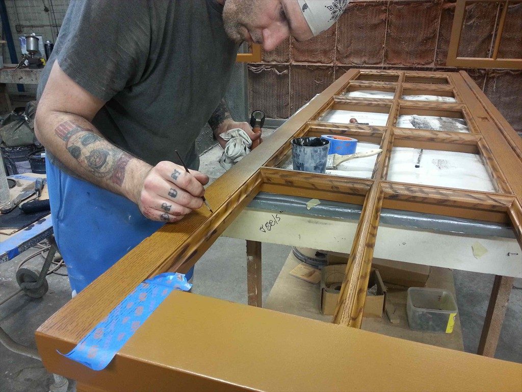 A worker applies a faux wood texture to a window frame.