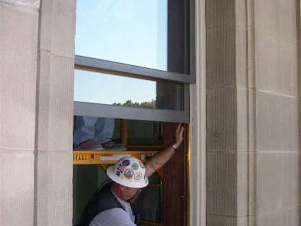 A worker braces a window frame during installation.