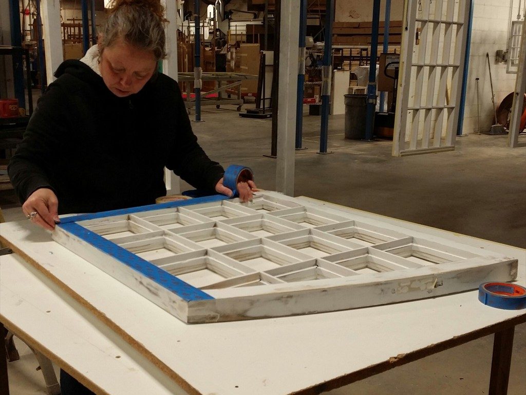 A worker applies masking tape to a window sash.